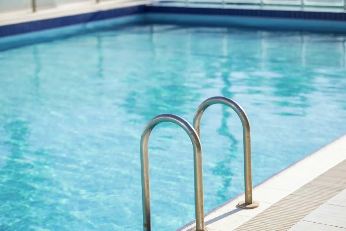 Corrimão de aço inox descendo para dentro de uma piscina de água azul clara e transparente.
