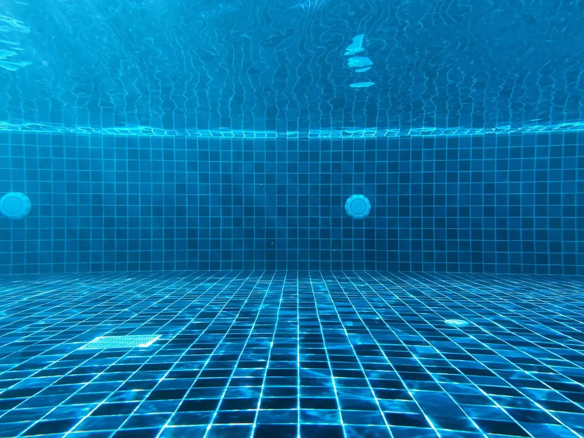 Fundo de piscina revestido de azulejo azul, visto de dentro d'água, com o ralo ao centro.