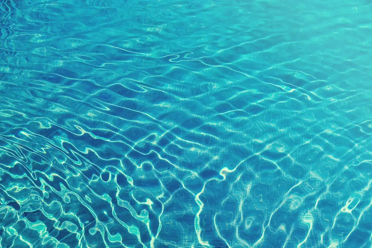 Luz do sol refletida na superfície ondulada de uma piscina de água azul clara.